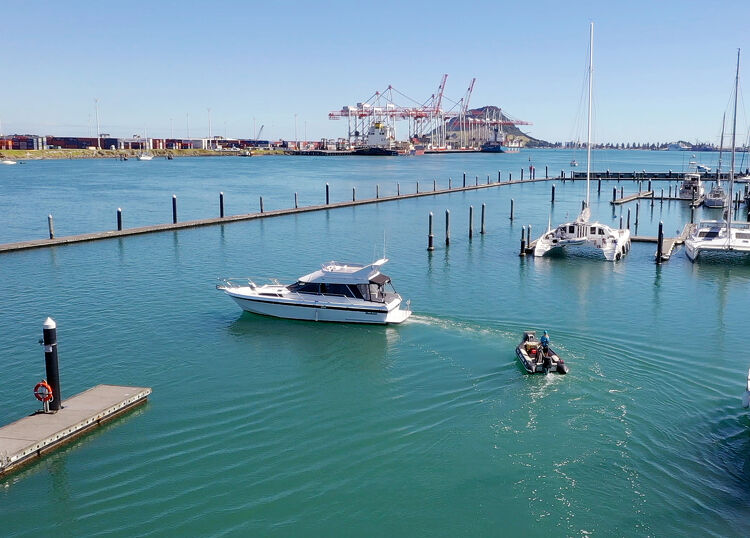 Boats cruising through Tauranga Harbour near the port and marina, with container cranes in the background, Bay of Plenty, New Zealand.